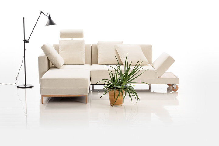 Cremefarbenes Sofa von brühl mit Holzelementen und Rollen an der Rückenlehne.