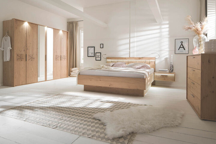 Helles Schlafzimmer mit Holzbettrahmen von Casada, verstellbaren Wandleuchten, Nachttisch und einem großen Kleiderschrank mit Holzdetails.