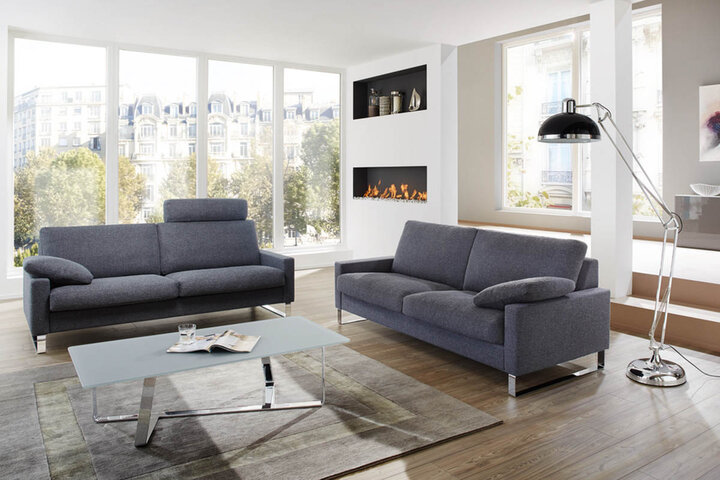 Wohnzimmer mit schwarzem Ledersofa von Erpo, einem eleganten Kaffeetisch und einer modernen Stehlampe. Der Raum ist lichtdurchflutet durch große Fenster.