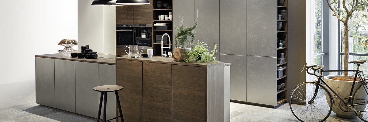 Moderne Nolte-Küche mit mattgrauen Fronten, Holzdetails, Kücheninsel mit Spüle, offenen Regalen und zwei schwarzen Pendelleuchten.