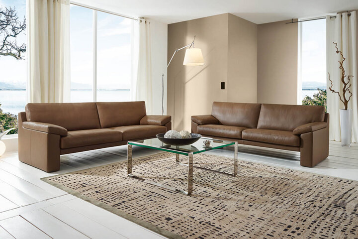 Modernes Wohnzimmer mit grünem Sofa von Erpo, runden Couchtischen und einer großen Fensterfront, die eine helle und offene Atmosphäre schafft.