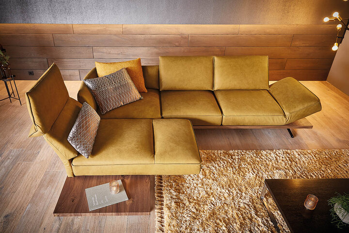Designorientiertes Sofa von KOINOR in warmem Cognac-Leder mit filigranen Metallfüßen – modern in Szene gesetzt mit Glas-Couchtisch und natürlichem Lichteinfall.