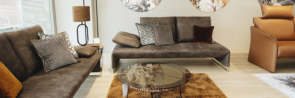 Wohnzimmer mit zwei Sofas, einem runden Glastisch, Stehlampe und drei runden Wandbildern mit floralen Motiven.