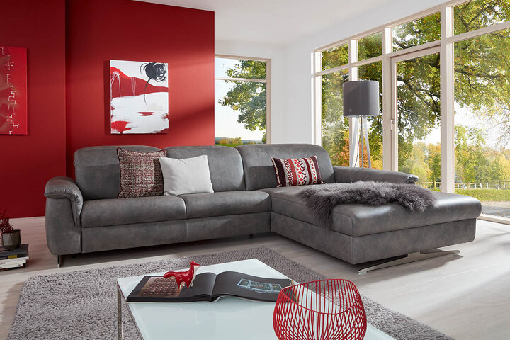 Großzügige Wohnlandschaft von himolla in grauem Lederlook mit Recamiere, dekorativen Kissen und kuscheliger Decke – modern in Szene gesetzt vor roter Akzentwand und großen Panoramafenstern.