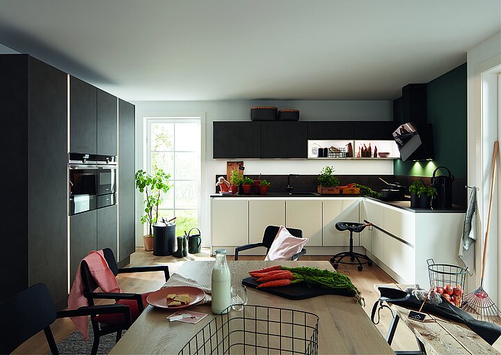 Moderne Nolte-Küche mit L-förmiger Arbeitsfläche, weißen und dunklen Fronten, integriertem Backofen, Holzarbeitsplatte und Sitzbereich mit Stühlen und Hockern.