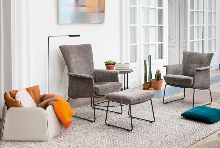 Zwei stilvolle Sessel mit Hocker von JORI in hellem Grauton, kombiniert mit filigranem Metallgestell – wohnlich ergänzt durch Pflanzen, Kissen und moderne Deko-Elemente.
