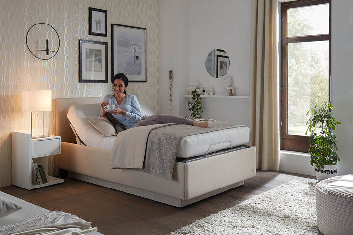 RUF Designerbett mit grauem Stoffbezug, breitem Kopfteil und wohnlicher Atmosphäre durch dezente Accessoires.
