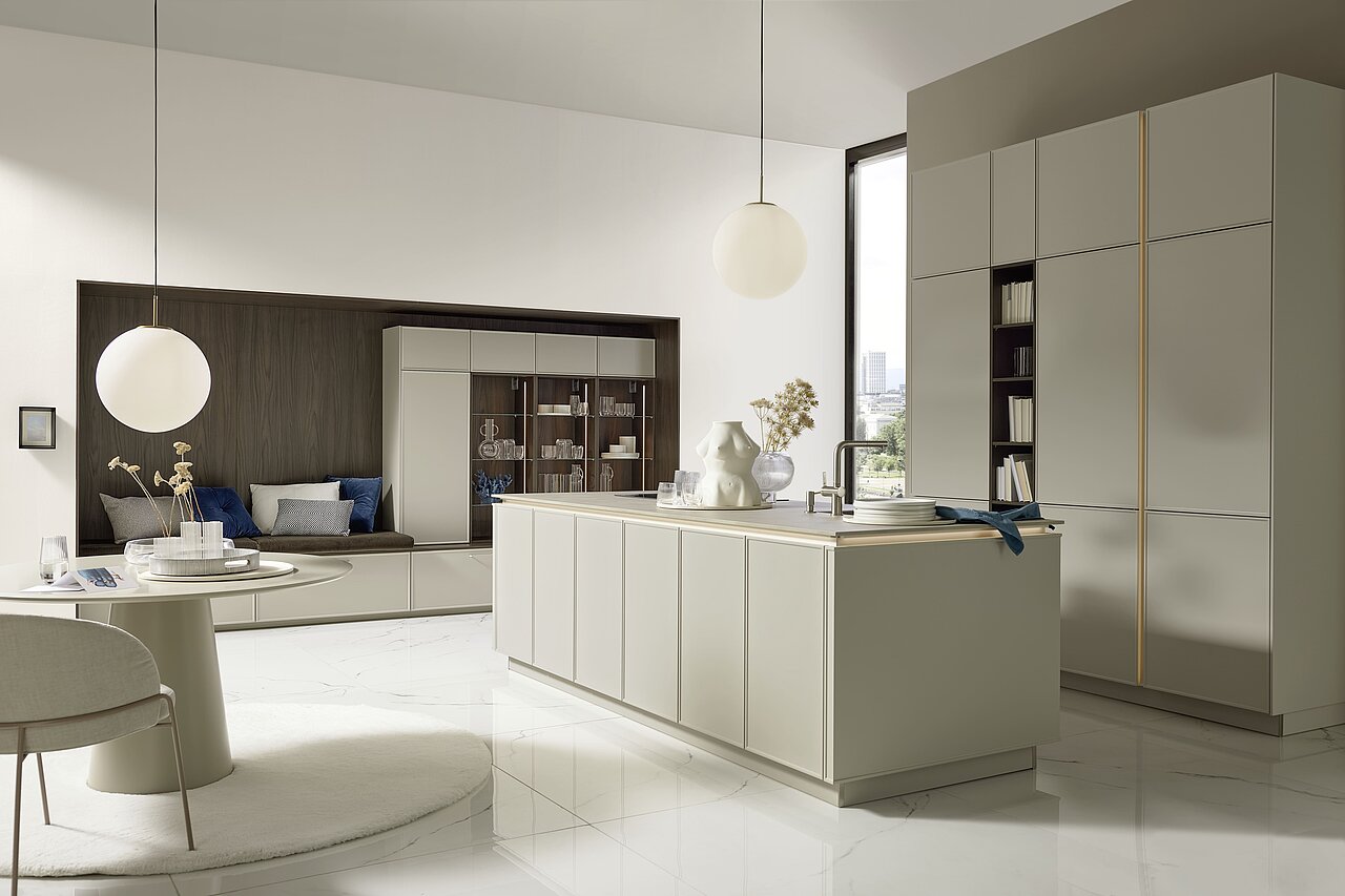 Elegante Nolte Küche EVORA LACK in Greige softmatt mit Kochinsel, beleuchteter Glasvitrine und Marmorboden.