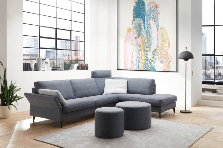 Graues Wohnzimmer mit Sofa und Sesseln von Erpo, Tisch mit Zeitschriften und einer modernen Stehlampe. Der Raum hat große Fenster mit einem Blick auf eine städtische Szenerie.