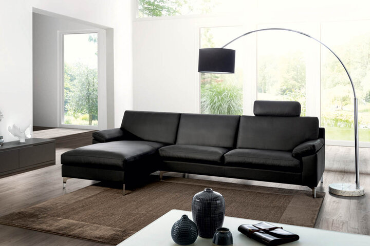 Wohnzimmer mit schwarzem Ledersofa von Erpo, einem großen Kaffeetisch und modernen Fenstern, die den Blick auf einen Garten freigeben.
