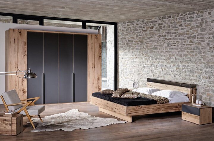 VOGLAUER-Bett mit markanter Holzmaserung und klarer Linienführung – kombiniert mit passendem Nachttisch, stimmungsvoller Beleuchtung und sanften Textilien.