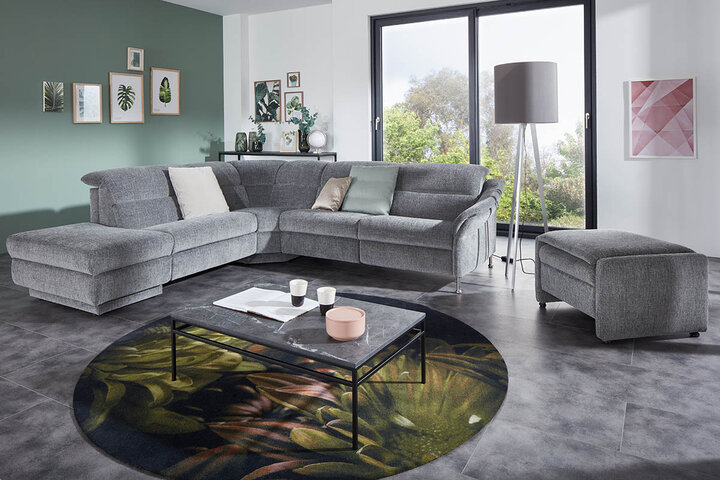 Moderne, hellgraue Wohnlandschaft von himolla in L-Form mit verstellbaren Kopfteilen, passendem Hocker und stimmiger Wandgestaltung im Naturmotiv-Stil.